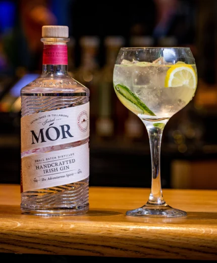A bottle of handcrafted Irish gin beside a refreshing cocktail on a wooden bar.