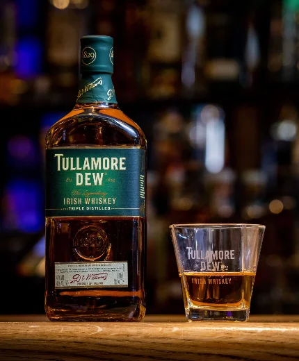 A bottle of Tullamore D.E.W. and a glass filled with whiskey on a cosy bar counter.