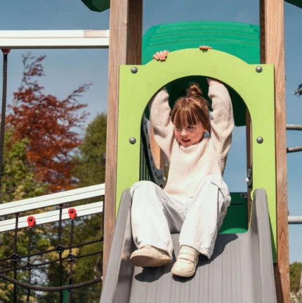 A young girl joyfully slides down a playground slide on a sunny day.