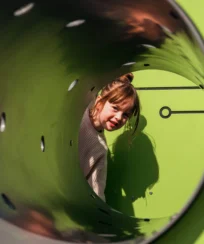 Child smiling inside a green play tunnel at a resort playground.