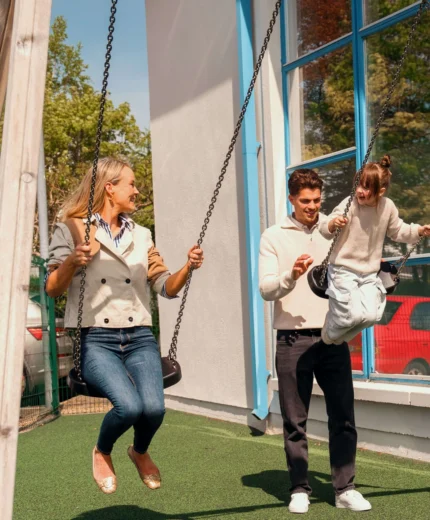 A cheerful family enjoys playing on swings at a sunny resort playground.