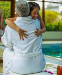 Family embracing by a resort pool in bathrobes, smiling and enjoying a sunny holiday.