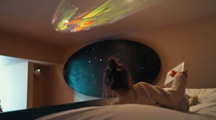 A child gazes at stars projected on a cosy hotel room ceiling.