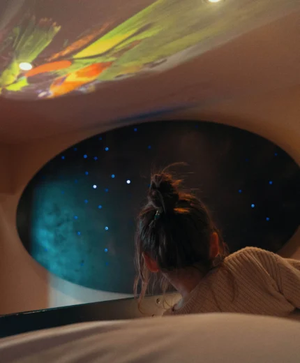A child gazes at stars projected on a cosy hotel room ceiling.