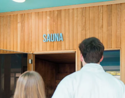 A couple in robes approaches a cosy sauna room at a hotel resort.