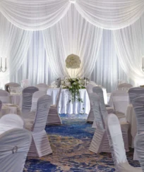 Elegant wedding reception setup with white drapery, round tables, and floral centrepieces.