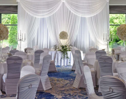 Elegant wedding reception setup with white drapery, round tables, and floral centrepieces.