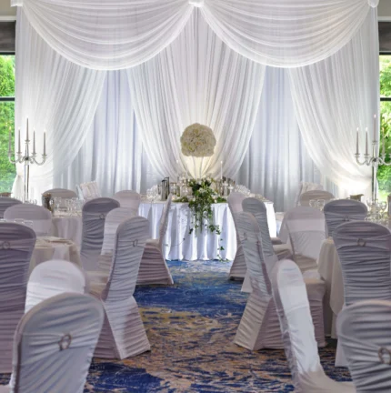 Elegant wedding reception setup with white drapery, round tables, and floral centrepieces.