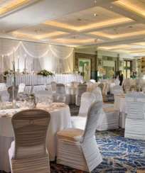 Elegant dining hall setup for a wedding reception with round tables and white chairs.