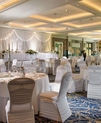 Elegant dining hall setup for a wedding reception with round tables and white chairs.