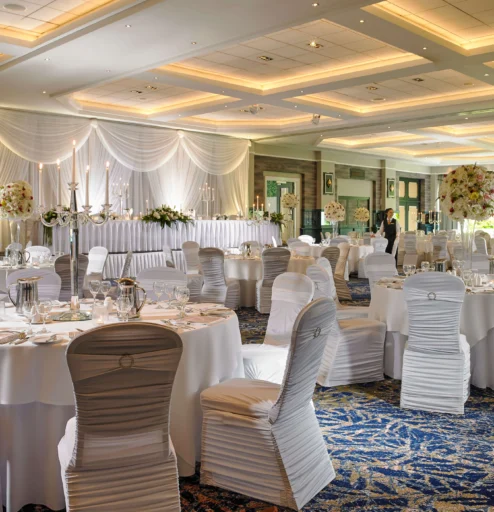 Elegant dining hall setup for a wedding reception with round tables and white chairs.