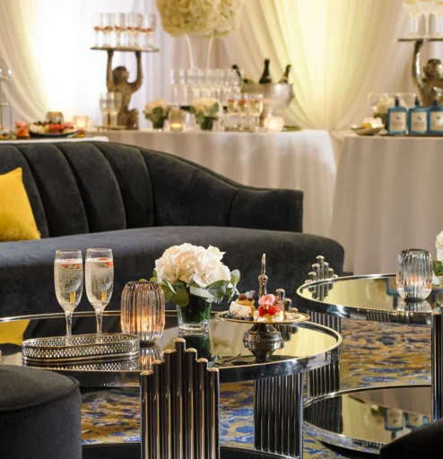 Elegant hotel lounge with plush seating, floral decor, and champagne glasses on tables.