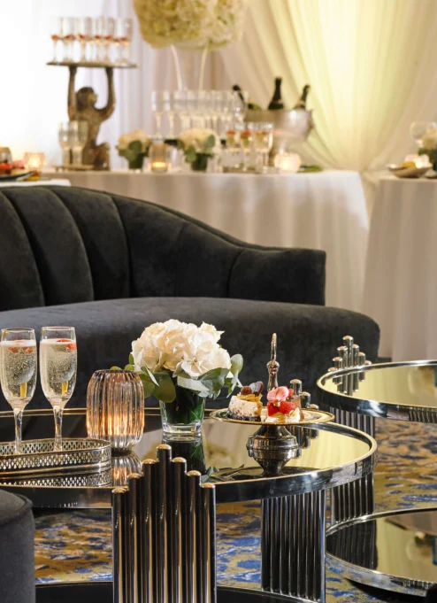 Elegant hotel lounge with plush seating, floral decor, and champagne glasses on tables.