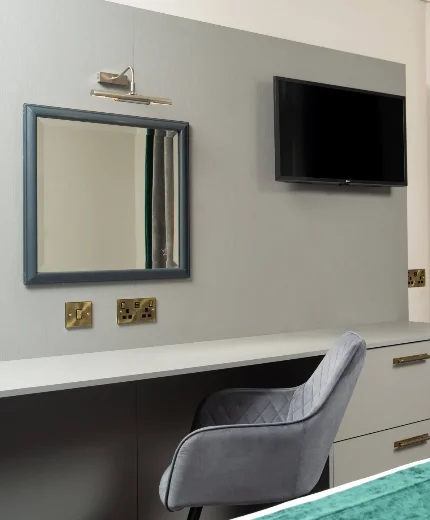 Elegant hotel room with desk, chair, and TV. Modern décor with green curtains and cosy bed.