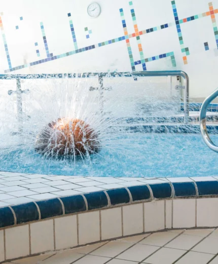 Family enjoying indoor pool with water fountain in hotel spa.