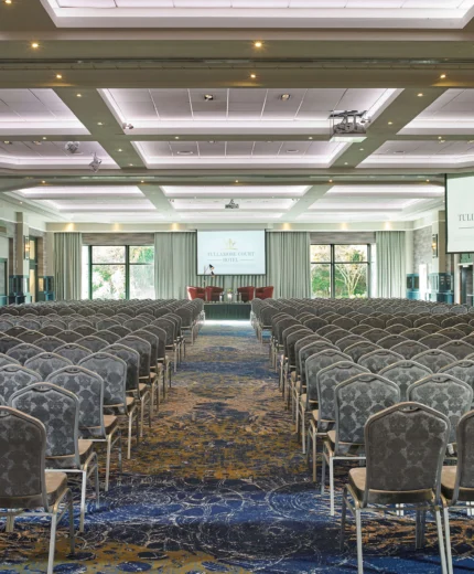 Elegant conference room in a hotel, set up for a large event with rows of chairs facing two screens.