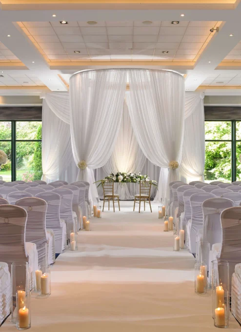 Elegant wedding venue with white drapery, chairs, and candlelit aisle.