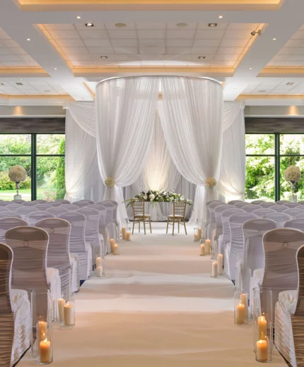 Elegant wedding venue setup with white drapes and candlelit aisle.