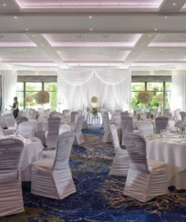 Elegant banquet hall set for a wedding with round tables, white linens, and floral centrepieces.
