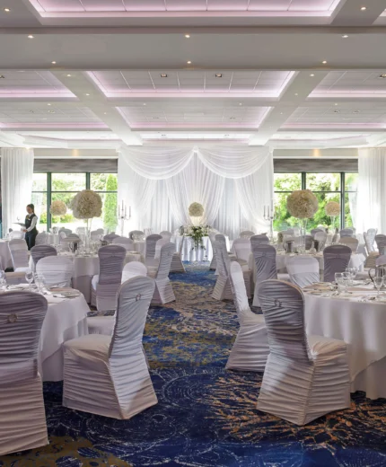 Elegant banquet hall set for a wedding with round tables, white linens, and floral centrepieces.