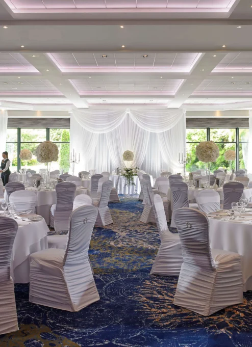 Elegant banquet hall set for a wedding with round tables, white linens, and floral centrepieces.