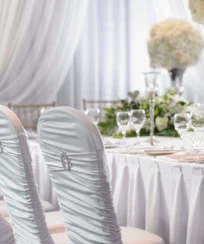 Elegant dining setup with white draped chairs and floral centrepieces in a resort setting.