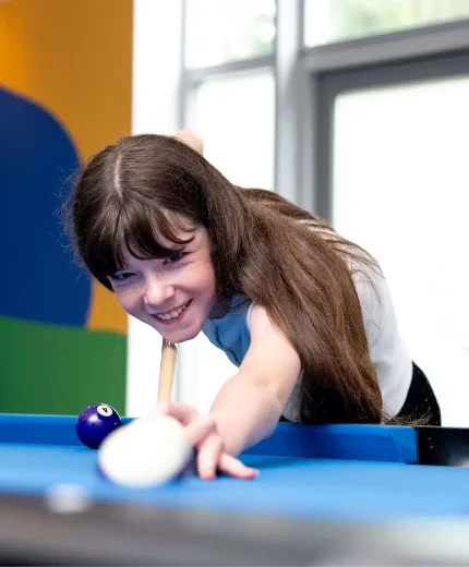 Young girl enjoying a game of pool in a colourful family-friendly resort setting.