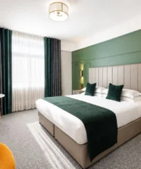 Modern hotel room with a double bed, green accents, and seating area, exuding comfort.
