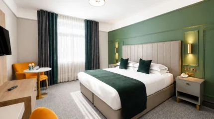 Modern hotel room with a double bed, green accents, and seating area, exuding comfort.
