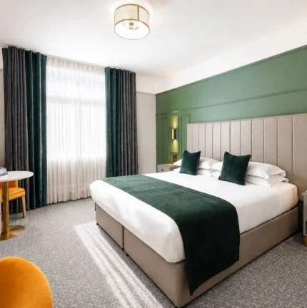 Modern hotel room with a double bed, green accents, and seating area, exuding comfort.