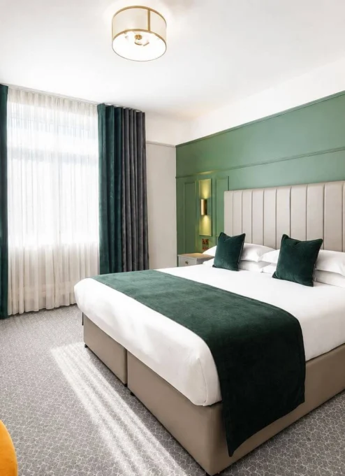Modern hotel room with a double bed, green accents, and seating area, exuding comfort.