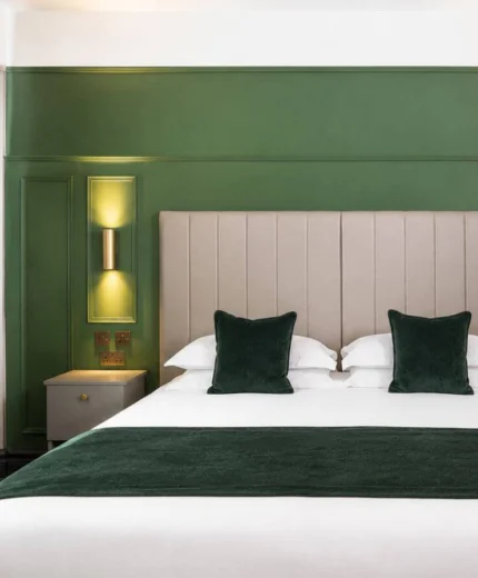 Elegant hotel room with a plush bed, green decor, and soft lighting, creating a relaxing atmosphere.