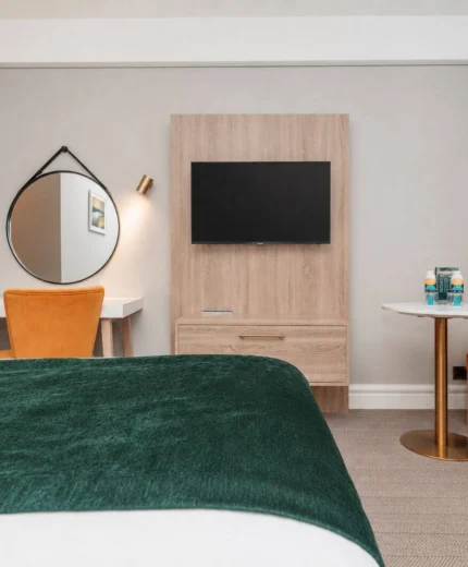 Cosy hotel room with a plush green bedspread, orange chairs, and a flat-screen TV.