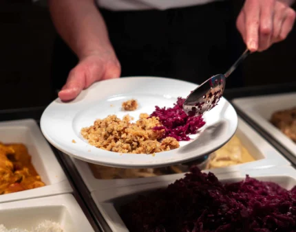Person serving food onto a plate at a buffet in a warm dining setting.