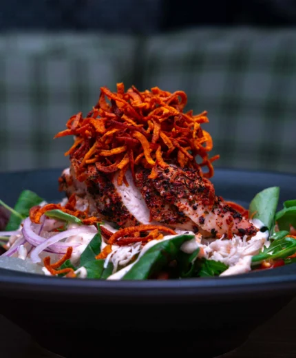 Grilled chicken salad with crispy toppings in a cosy restaurant setting.