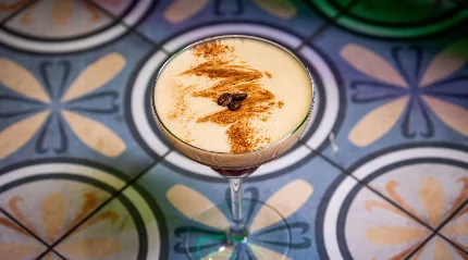 A creamy espresso martini with coffee beans, served on an ornate tile table.