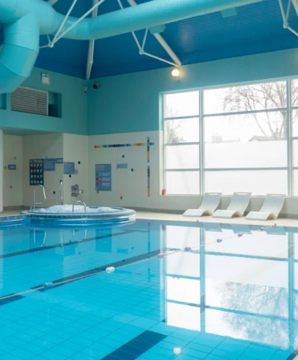 Indoor hotel pool with hot tub and sun loungers, illuminated by natural window light.