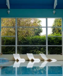 Indoor pool with loungers by large windows at a serene resort.