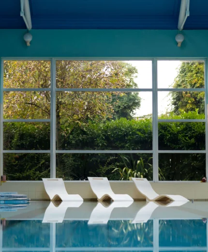 Indoor pool with loungers by large windows at a serene resort.