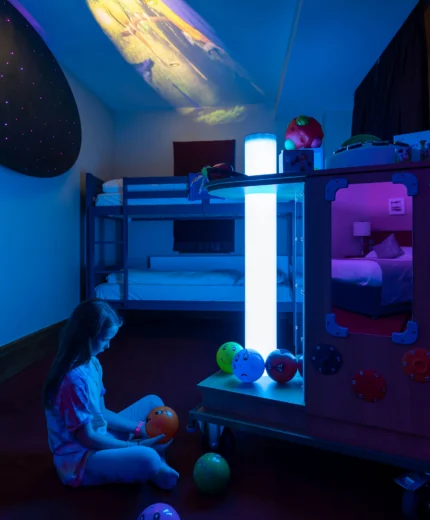Child in colourful, cosy room with bunk bed and playful lighting.