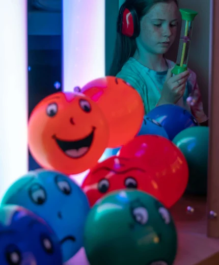 Child enjoying a colourful room with smiling balloons.