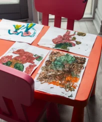 Children’s artwork displayed on a vibrant pink table with a pink chair nearby.