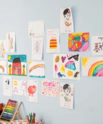 Children's colourful drawings displayed on a light blue wall in a cosy play area.