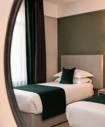 Cosy hotel room with two neatly made twin beds, green accents, and soft lighting.