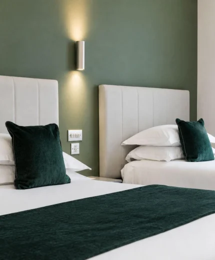 Cosy hotel room with twin beds and plush green accents, exuding comfort and elegance.