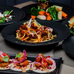 A variety of gourmet dishes served on black plates, showcasing colourful, fresh ingredients.