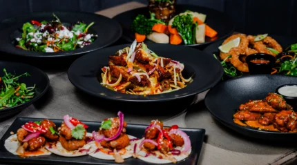 A variety of gourmet dishes served on black plates, showcasing colourful, fresh ingredients.