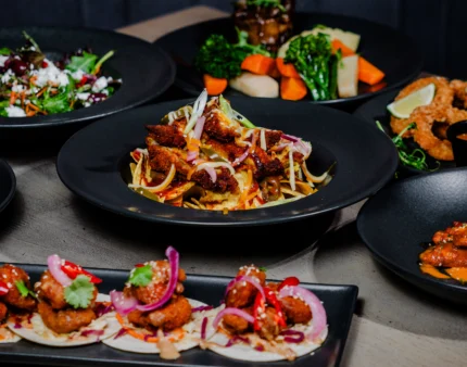 A variety of gourmet dishes served on black plates, showcasing colourful, fresh ingredients.