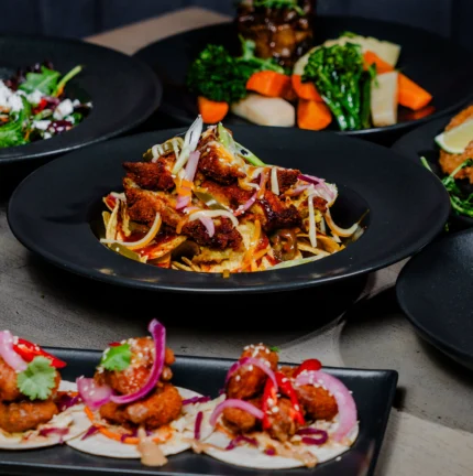 A variety of gourmet dishes served on black plates, showcasing colourful, fresh ingredients.