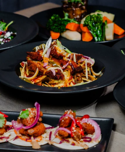 A variety of gourmet dishes served on black plates, showcasing colourful, fresh ingredients.
